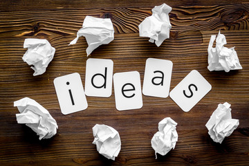 Writer's block concept. Ideas text among crumpled paper on dark wooden background top-down