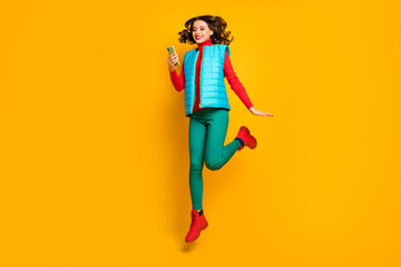 Full size photo of cheerful cute girl jump use cellphone social media repost sales news wear red blue green pants trousers isolated over yellow color background