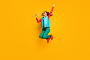 Full length photo crazy ecstatic girl use smartphone read social network discount win lottery jump raise fists scream wear red blue green pants vest footwear isolated bright color background