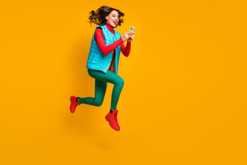 Fototapeta na wymiar Full length profile side photo energetic crazy blogger girl jump use smartphone follow autumn season discount run wear red blue green pants trousers vest boots isolated bright color background