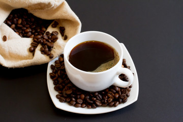 coffee beans in a bag with a white Cup of fresh coffee on a black background. space for text, top view.