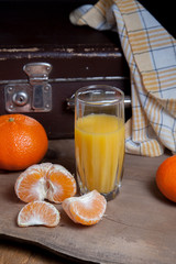 Unpeeled round ripe orange mandarins or tangerines, slices of peeled mandarin and glass of fresh juice on wooden board.