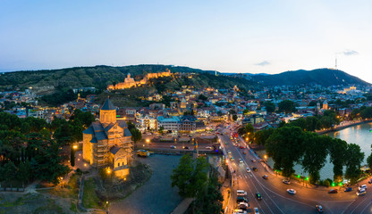 The evening panorama of the old town in the old district of Avlabari, Holy Trinity Cathedral and Rike Park, the Kura river reflects the evening city lights in Tbilisi, Georgia. © miklyxa