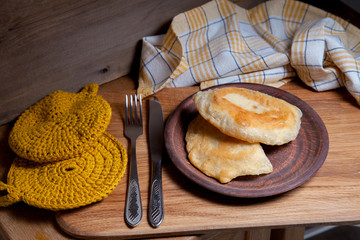 Clay plate of fried meat pies with cutlery on wooden table.