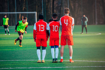 Fototapeta premium Football free kick, soccer concept photo, players in red jerseys, green grass sunset light