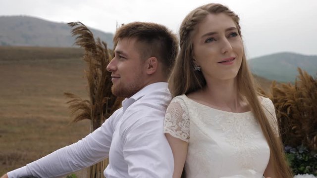bride smiles sitting near muscular fiance at stylish brown decorations against hilly landscape slow motion closeup