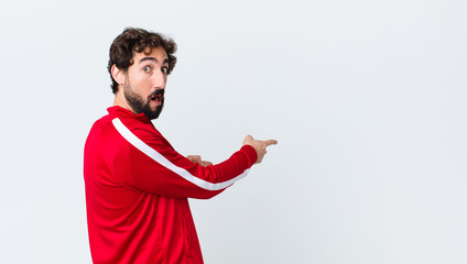 young bearded man back view feeling shocked and surprised, pointing to copy space on the side with...