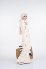 A beautiful Muslim female model in a Asian traditional dress kurung Pahang carrying shopping bags isolated on white background. Eidul fitri festive preparation shopping concept. Full length portrait.