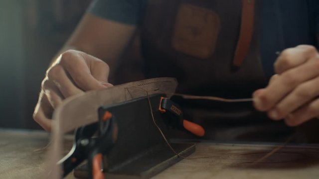Medium shot of artisan's hands stiching a handmade leather belt