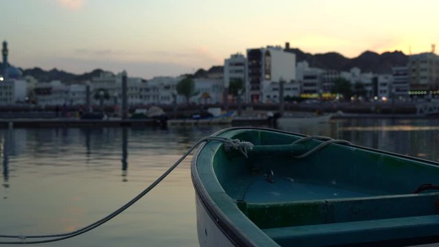 a parked boat tied to a dock with the city in the background. Muscat, Oman