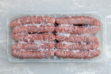 frozen sausages in plastic box on ceramic background