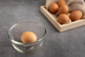Chicken eggs on the wooden tray and glass bowl on the black cement floor. High angle view.