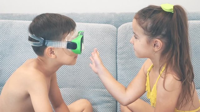 Boy and girl wearing swimming suits are sitting is a sofa. Girl is cheching wether boy sees something. Close up. Copy space. 4K.