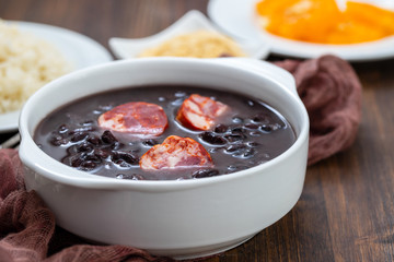 typical brazilian food black beans with smoked sausages in white bowl