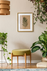 Vintage interior design of living room with design retro pouf , pendant lamp, plants, cacti, decoration and gold mock up poster frame on the beige wall. Stylish home decor. Retro concept. Template. 