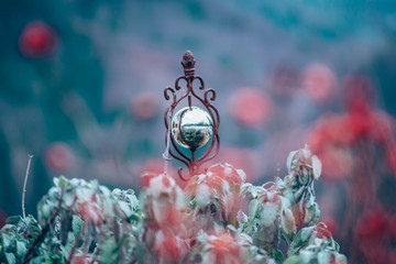 Artistic garden ornament featuring a reflective metal sphere suspended in ornate metalwork. Soft-focus background and pastel tones create a dreamy outdoor atmosphere.