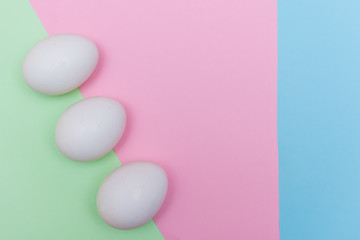 Three Easter holiday flat lay with white egg on a solid light green, blue, and pink pastel background with copy space.