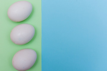 Three Easter holiday flat lay with white egg on a solid light green and blue pastel background with copy space.
