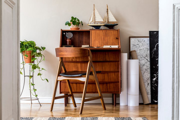 Stylish and vintage interior design of living room with wooden retro commode, plants, ships, chair, maps and elegant personal accessories. Mock up poster frame on the wall. Template. Home decor.