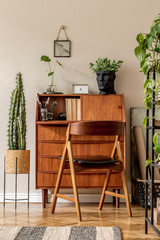 Retro interior design of art workshop room with wooden vintage bureau and chair, shelf plants, cacti, books, photos and elegant personal accessories. Stylish vintage home decor. Beige wall. Template. 