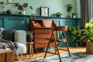 Stylish interior design with retro wooden cabinet, chair, mint sofa, a lot of plants, vintage clock, decoratnion and elegant personal accessories. Modern retro concept of home office space. Template.