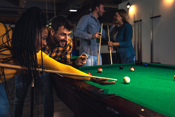 Group of cheerful friends playing billiard together in bar.