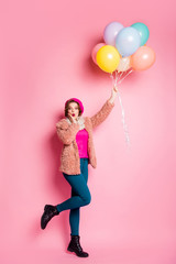 Full size vertical photo of funny pretty lady hold many colorful balloons flying up air crazy wear modern fur coat scarf beret cap trousers shoes isolated pink color background