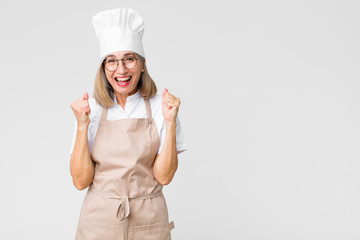 middle age baker woman feeling shocked, excited and happy, laughing and celebrating success, saying...
