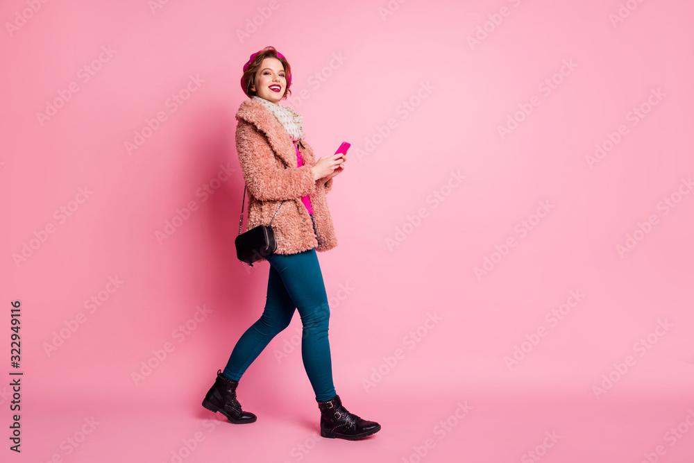 Wall mural Full length profile photo of pretty lady hold telephone chatting friends walking down street wear casual stylish fur coat scarf beret trousers shoes isolated pink color background