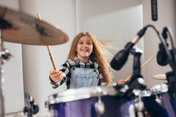 Obraz na płótnie Canvas young girl playing drums in music studio