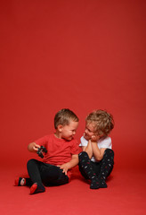 Two little boys sit on a red background