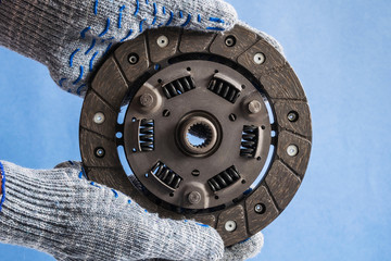 Hands of the master holds a clutch disc on a blue background.