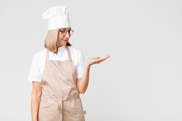 middle age baker woman feeling happy and smiling casually, looking to an object or concept held on...
