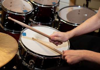 Closeup of a pair of hands with drumsticks playing a drum set.