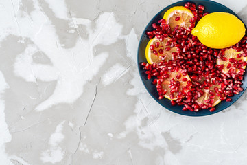 yellow lemon slices sprinkled with red pomegranate seeds in a blue ceramic dish on a textured gray background
