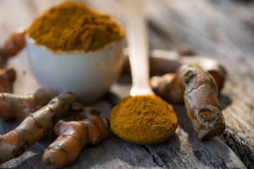 Turmeric powder and fresh turmeric in wood bowls on wooden table.