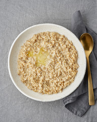 Whole oatmeal, large bowl of porridge with butter for breakfast, morning meal. Top view