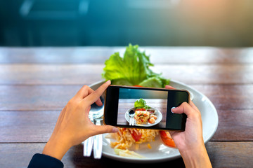 Hand holding mobile phone and take a photo Fried rice with spicy shrimp on blurred wooden table ...