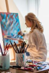 Art painter working on her abstract paintings at workshop. Selective focus on paintbrushes, palette...