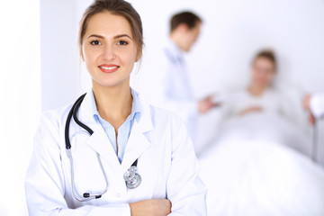 Fototapeta premium Female doctor smiling on the background with patient in the bed and two doctors