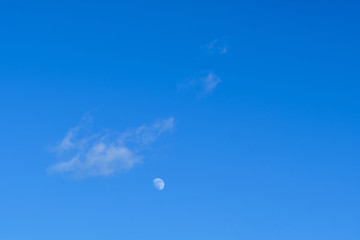 Clear blue sky with a white cloud an the moon as background with copy space. Seen in Bavaria, Germany on a sunny February day