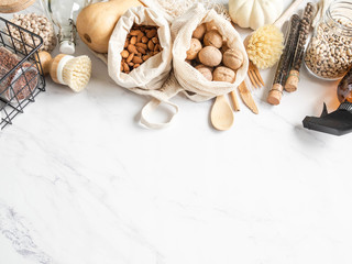 Zero waste concept. Flat lay eco-friendly kitchen set. Food, brushes, wood appliances, bags, bottle and jar, spices in glass tubes on marble background. Top view. copy space