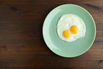 fried eggs on a plate on dark wooden background flat lay.
