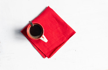 Cup of black coffee with spoon on red textile cover on white concrete background 