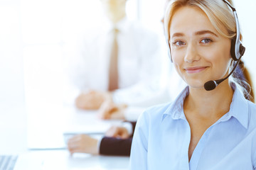 Group of diverse phone operators at work in sunny office. Handsome business woman with headphones...
