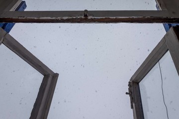 an old open window with a crack in the glass and falling snow