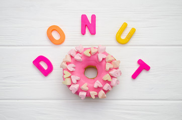 Sweet pink donut with icing and decoration with hearts on a white wooden background and with text letters