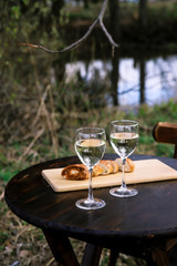 Spring picnic on nature – white wine in glasses and grill bread on wooden round table