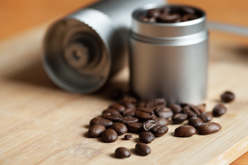 Coffee beans are on wooden desk near coffee grinder