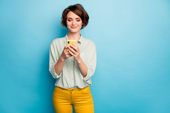 Photo of pretty lady holding telephone hands reading new blog post positive comments popular blogger wear casual green shirt yellow trousers isolated blue color background